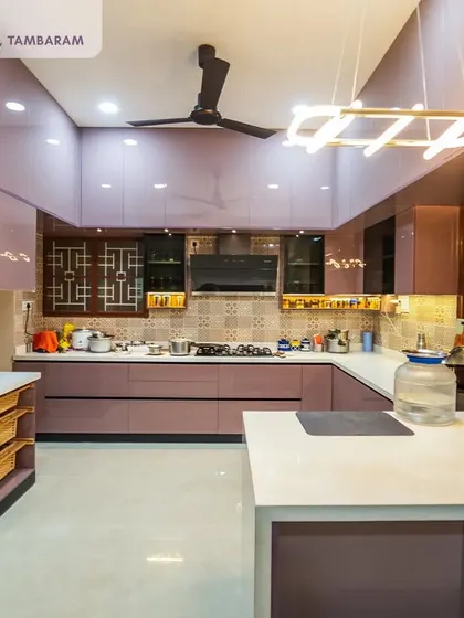 This spacious U-shaped kitchen in a Tambaram villa uses a beautiful mauve high-gloss laminate. The design includes an island counter, ample storage, and intricate CNC cutting details on the overhead cabinets, creating a truly luxurious feel.