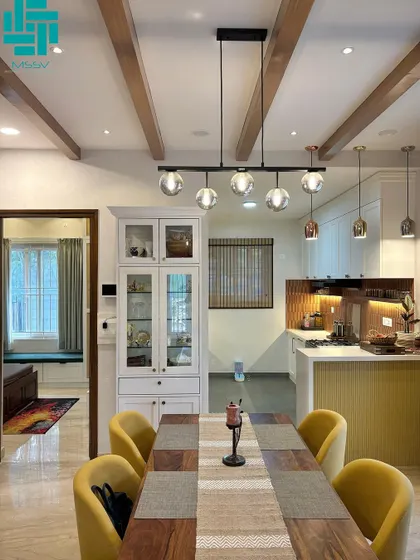 The dining area features a solid wood table with mustard yellow chairs, set under a modern chandelier with glass globes. The open layout connects it to the kitchen, making it ideal for hosting.