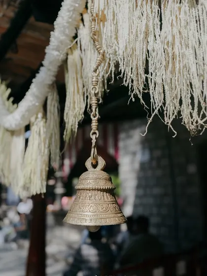 A traditional brass temple bell hanging from a floral garland. The sound of bells adds a serene and spiritual dimension to the wedding ceremony.