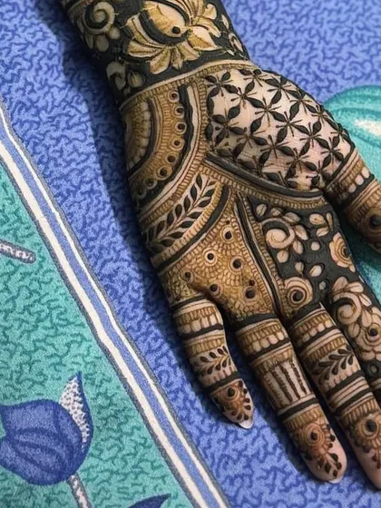 A close-up of a palm with extremely fine and dense henna work, featuring geometric and floral patterns.