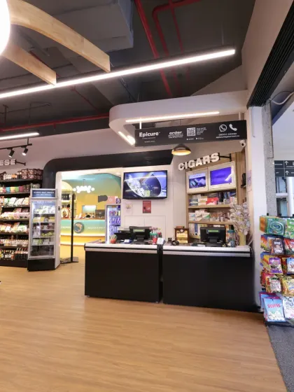 The checkout counter at Epicure is designed for efficiency and to showcase last-minute purchase items like cigars and snacks. The overhead lighting and clear branding ensure a smooth and pleasant end to the shopping experience.