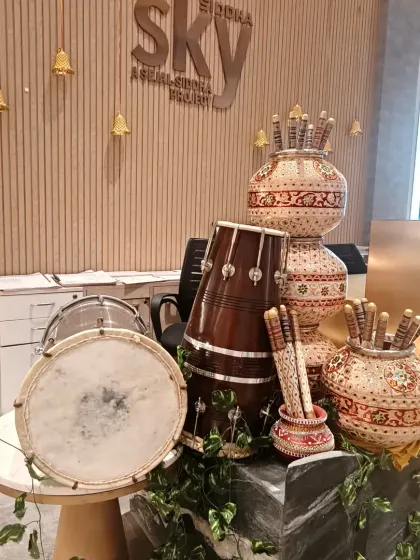 Traditional decor elements for a Navratri celebration in a building lobby. This corner features painted pots (matkas), dandiya sticks, and a dhol, setting the festive mood.