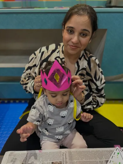 A mother places a paper crown on her child's head that they made together, a sweet moment of pretend play and accomplishment.