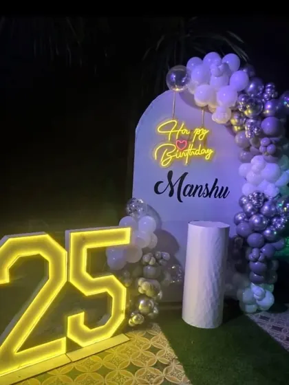 An outdoor 25th birthday party at night, with a balloon arch and large, glowing marquee numbers.