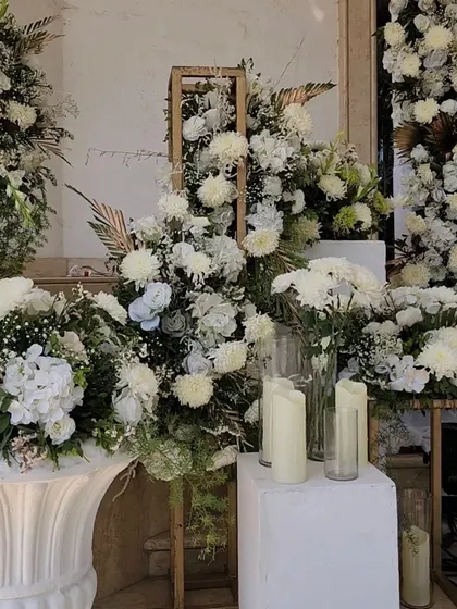 A lavish display of white flowers in various arrangements, using wooden frames and classic white urns to create a stunning photo corner.