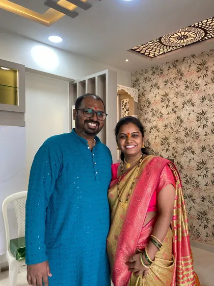 A beautiful portrait of the Pakhare couple in their newly designed home, with a stunning custom mandir and ceiling design in the background.