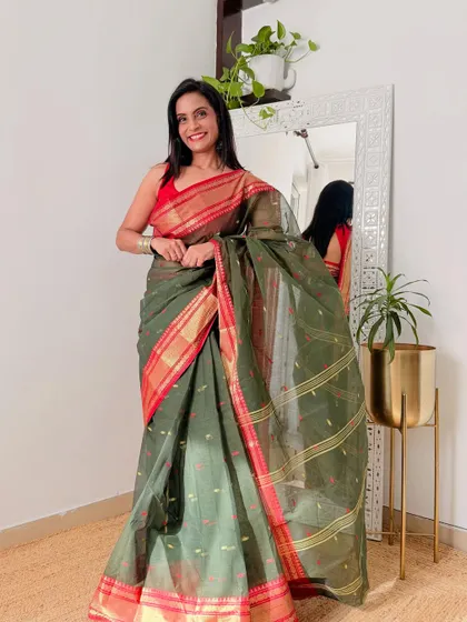 An olive green Tant saree with a rich red and gold border. This is a classic combination that looks very elegant and is perfect for a formal or festive occasion.