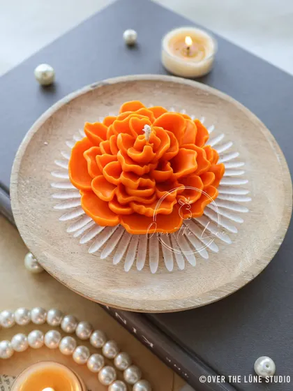 An orange Camellia floating candle placed on a wooden dish. Even on its own, it makes a beautiful, minimalist decor piece. The vibrant color is perfect for adding a pop of warmth.