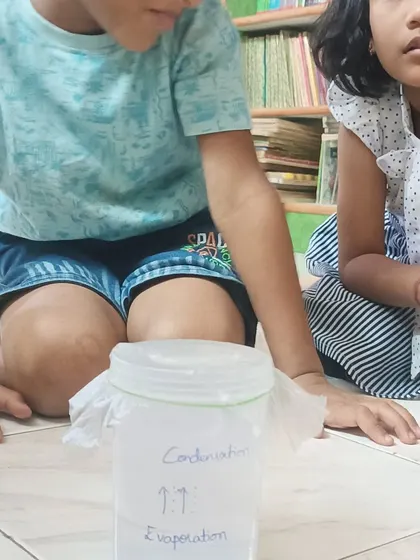 Students observe the water cycle experiment, learning about evaporation and condensation.