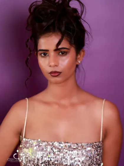 A direct and confident portrait against a purple background. The lighting is clean, and her expression is powerful.
