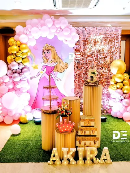 A glamorous princess theme for Akira's 5th birthday. This setup features a large cutout of Princess Aurora, a pink sequin backdrop, and a stunning balloon arrangement in shades of pink and gold.