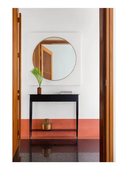 A view of the entry interface, featuring a sleek console table I designed. The piece is crafted from black powdered metal, providing a sharp, graphic contrast to the warm wood doors and terracotta floor.