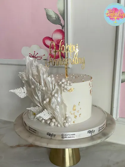 A pristine white anniversary cake with delicate, abstract white sails and pearl details.