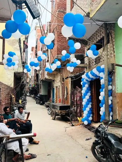 Outdoor decorations for a 'Welcome Baby' event. The entire street lane is decorated with blue and white balloon clusters, announcing the celebration to the neighborhood.
