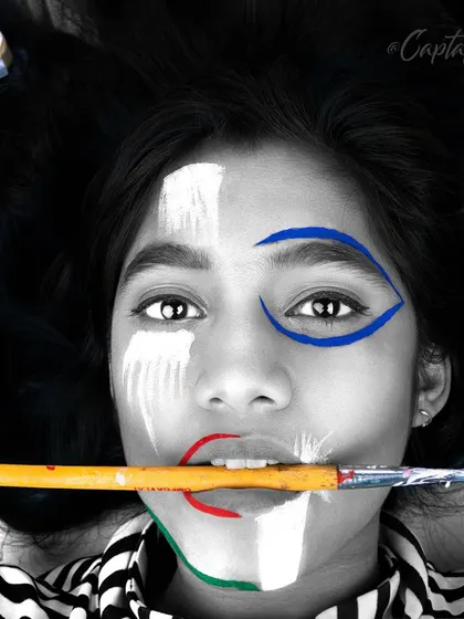 A striking black and white photo with selective color, this image plays with contrast and composition. The direct gaze and the paintbrush held in the mouth make for a bold and unconventional creative portrait.