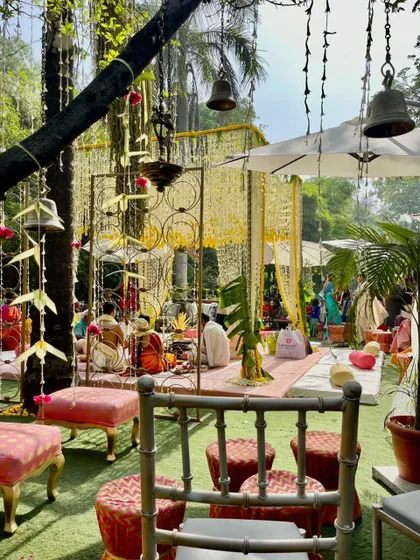 A beautiful daytime wedding ceremony in progress, showing the open-air mandap setup surrounded by lush greenery.