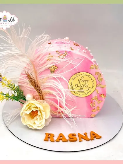 A unique and artistic dome-shaped cake for Rasna's birthday, decorated with feathers, gold leaf, and dried flowers for a boho-luxe vibe.