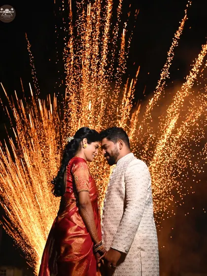 A close-up shot of a couple surrounded by the warm glow of fireworks. This photo captures the magical atmosphere of a wedding night celebration and the couple's happiness.