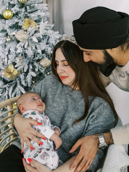 A family admiring their newborn baby by the Christmas tree. A baby's first Christmas is an incredibly special milestone to document.