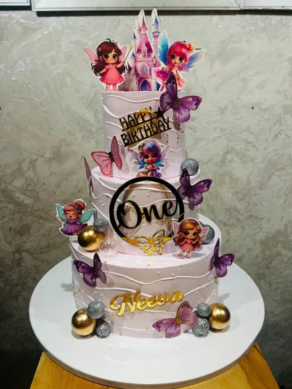 A whimsical three-tier fairy-themed cake for a first birthday, decorated with fluttering butterflies and sparkling gold and silver balls.