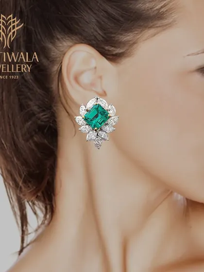 A pair of classic stud earrings featuring a large emerald surrounded by a floral halo of marquise diamonds. A timeless design that celebrates the beauty of this precious gemstone.