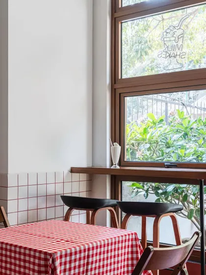We designed intimate window-side seating for solo diners or pairs. The wooden bar counter and high stools offer a view of the outdoors, while a milkshake on the sill hints at the classic diner experience we aimed to evoke.