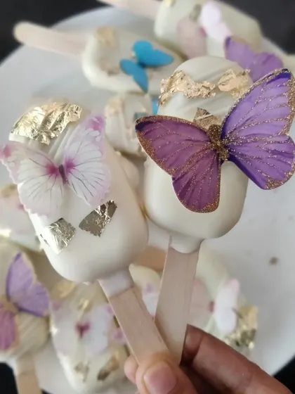 Our butterfly-themed cakesicles are a fun and delicious treat. A fudgy cake pop center is coated in white chocolate and adorned with edible butterflies and gold leaf.