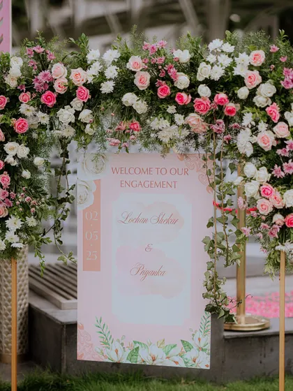 A beautiful floral arch frames the welcome sign for an engagement party. The lush pink and white roses create a romantic and inviting entrance for guests.