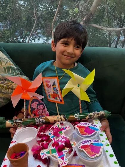 A smiling student holds up his Holi platter, complete with handmade decorations and treats.