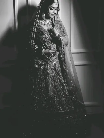 The same bridal portrait in black and white. This version emphasizes the texture of the lehenga and the play of light and shadow, giving it a classic, dramatic feel.