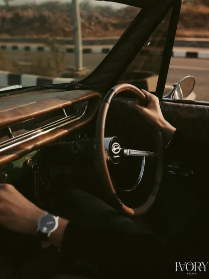 A detailed shot focusing on the groom's hands on the vintage wooden steering wheel. This image evokes a sense of journey and classic style, adding a storytelling element to their Goa pre-wedding shoot.
