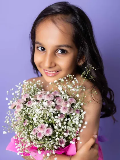 A close-up of her beautiful smile, holding the flowers close. The soft colors and creative concept make this a stunning and unique kid portrait.
