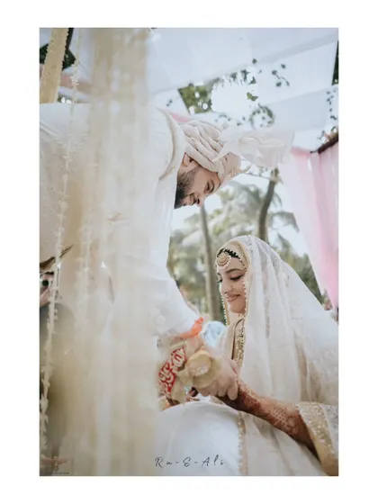 A tender moment of connection. The groom gently holds his bride's hand, their faces close, in a beautifully composed shot from their Nikaah ceremony.