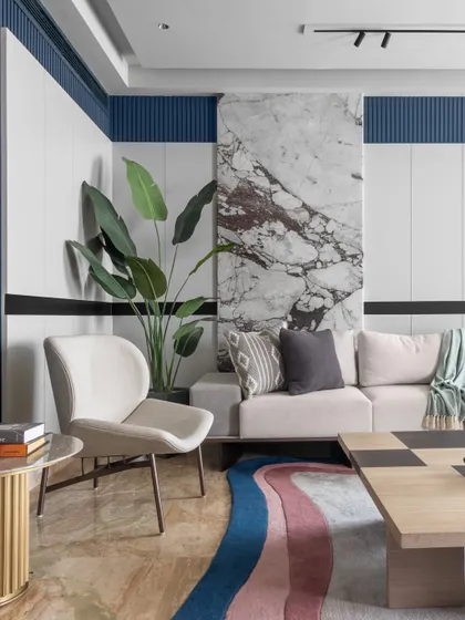 A close-up showing the material palette of the living room, including a statement marble wall, ribbed blue paneling, and a large indoor plant. These elements add texture, color, and a touch of nature to the modern design.