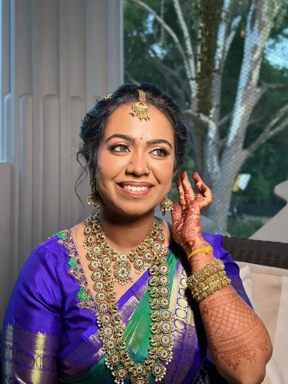 A smile that lights up the room. The radiant makeup, with its soft gold eyeshadow and rosy nude lip, enhances her joyful expression and complements the intricate bridal jewellery.