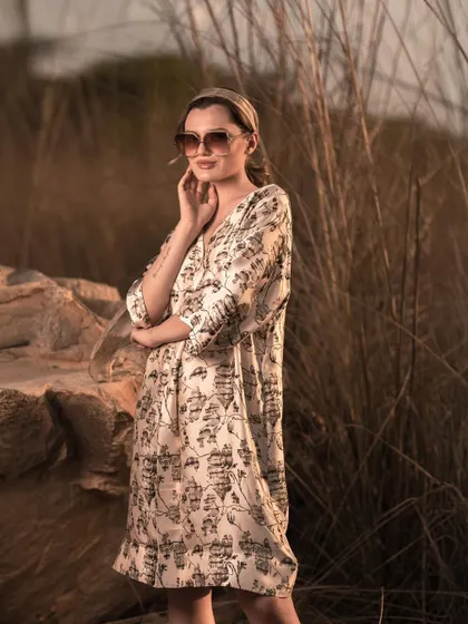 A relaxed, three-quarter shot of a model in a printed dress, set against tall, wild grass. The soft, natural lighting is ideal for showcasing resort wear and summer collections.