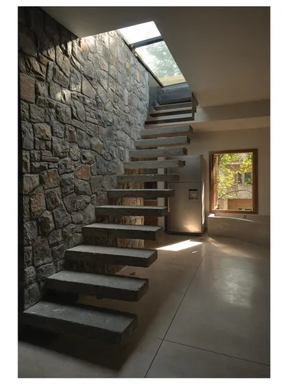This perspective highlights the dramatic play of sunlight from the skylight across the textured stone wall and floating concrete steps.