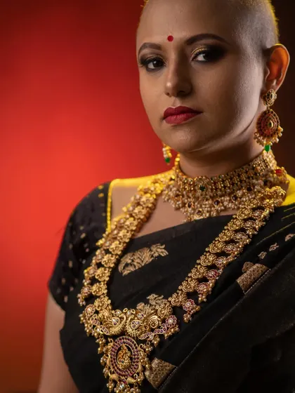 Pairing heavy, traditional gold jewellery with a bold, bald look for an empowering photoshoot. The makeup features a classic red lip and defined eyes to create a stunning contrast and celebrate unconventional beauty.
