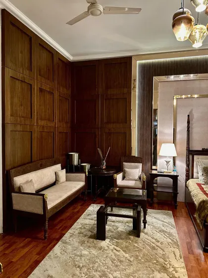 This view highlights the custom seating area within the bedroom, including a small sofa and armchair that match the room's elegant aesthetic. The dark wood wall paneling provides a rich, warm backdrop to the space.