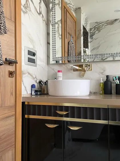 A detail shot of the Calacatta marble bathroom, showing the contrast between the black vanity, gold hardware, and the natural wood of the door. Every element is chosen to complement the overall theme.