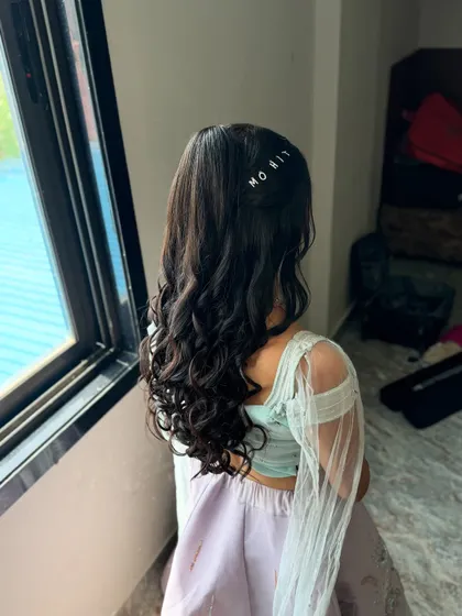 A close-up of this fun hairstyle for a Haldi carnival, featuring a high ponytail with soft curls and a personalized hair clip with the groom's name.