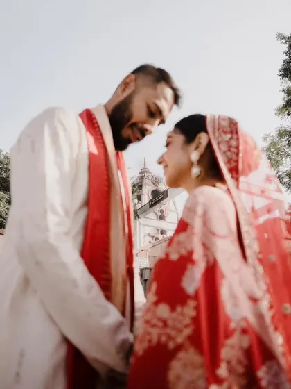 An artistic, low-angle shot of the bride and groom, capturing an intimate glance. The temple in the background adds a sense of tradition and sanctity.