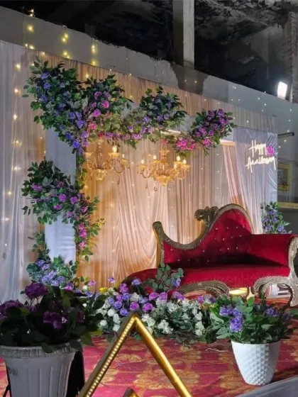 A unique anniversary decor featuring floral tree structures, chandeliers, and a classic red chaise lounge.