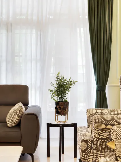 A detail shot of the living room, showing the comfy sofa next to the custom-printed armchairs and sheer curtains that let in plenty of natural light.