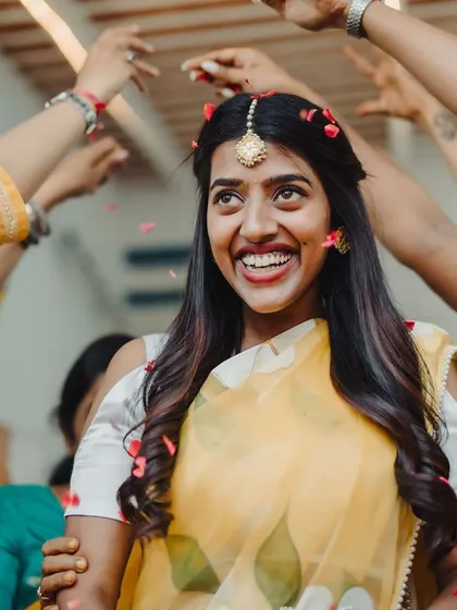 The bride, surrounded by the hands of her loved ones, enjoys a shower of flower petals during her Haldi.
