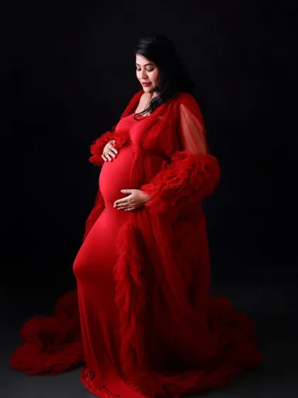 A classic portrait of a mom-to-be in a striking red ruffled gown against a solid black background, making the color and texture pop.