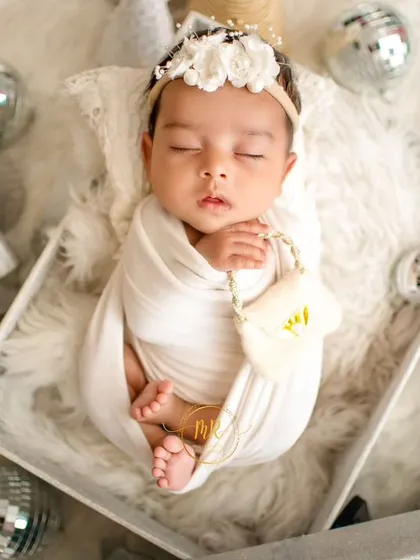 A newborn baby sleeps in a gift box, surrounded by silver and white Christmas decorations for a festive holiday portrait.