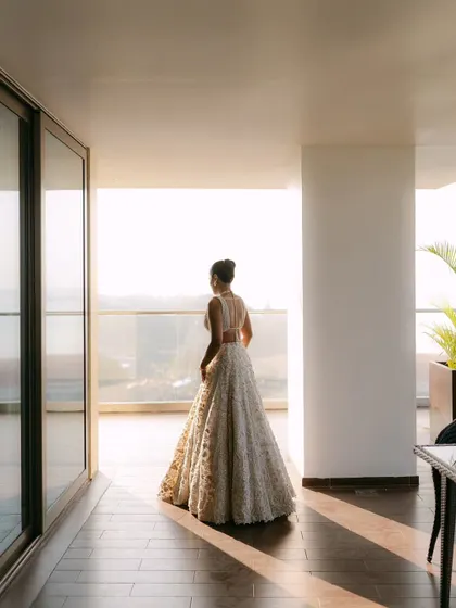 A bride stands on a balcony, looking out at the view. The backlighting and her elegant silhouette create a sense of anticipation and hope for the future.