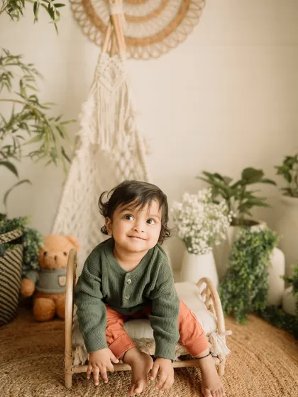 A sweet, calm portrait of a toddler sitting on the prop bed, looking up with a gentle smile.