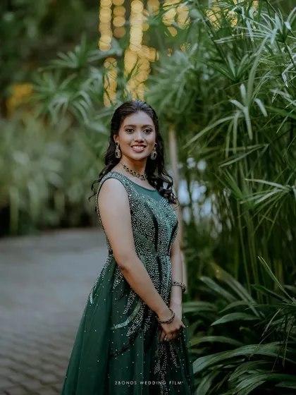 A beautiful portrait of the bride in her green reception gown, smiling against a backdrop of lush greenery.